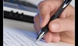 Professional Writing A hand holding a pen fills out a printed form on a desk, with part of a keyboard visible in the background.