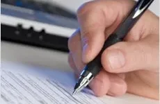Professional Writing A hand holding a pen fills out a printed form on a desk, with part of a keyboard visible in the background.