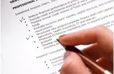 Professional Editing A hand holding a pen is poised over a printed resume, highlighting the professional experience section.